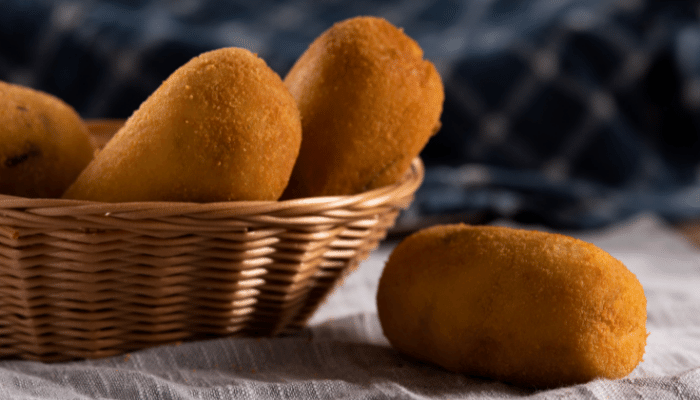 bolinho de mandioca recheado frito com 3 unidades dentro de uma pequena cesta e um fora da cesta ao lado