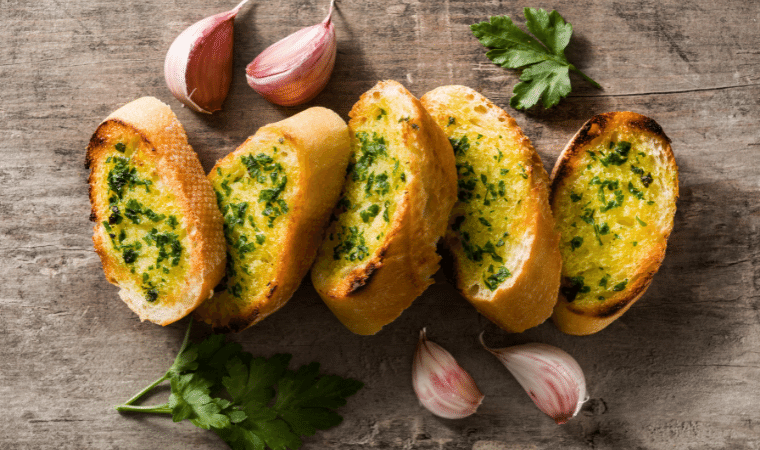 5 fatias de pão de alho com 4 dentes de alho e 2 folhas de cheiro verde decorando a imagem