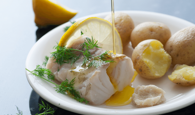 receita de bacalhau com batata servido em um prato branco e um fio de azeite em cima da posta de bacalhau