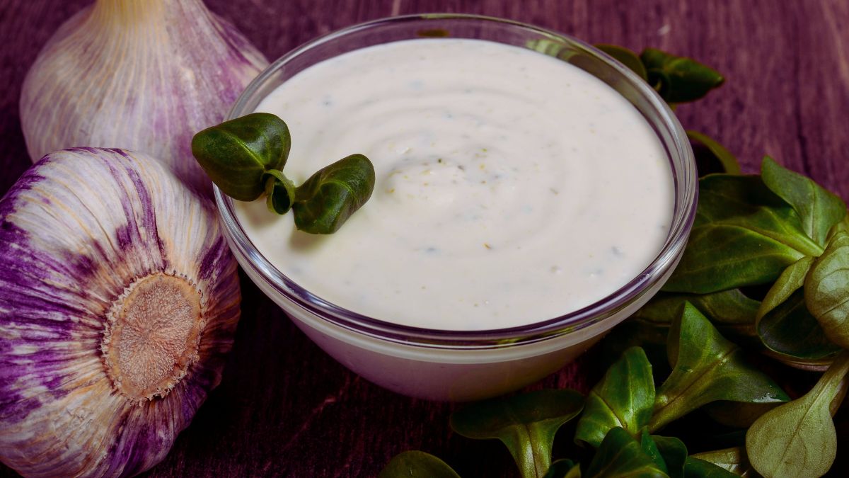 Molho de Alho Caseiro para Churrasco Perfeito servido numa travessa redonda de vidro com cabeças de alhos decorativas ao lado